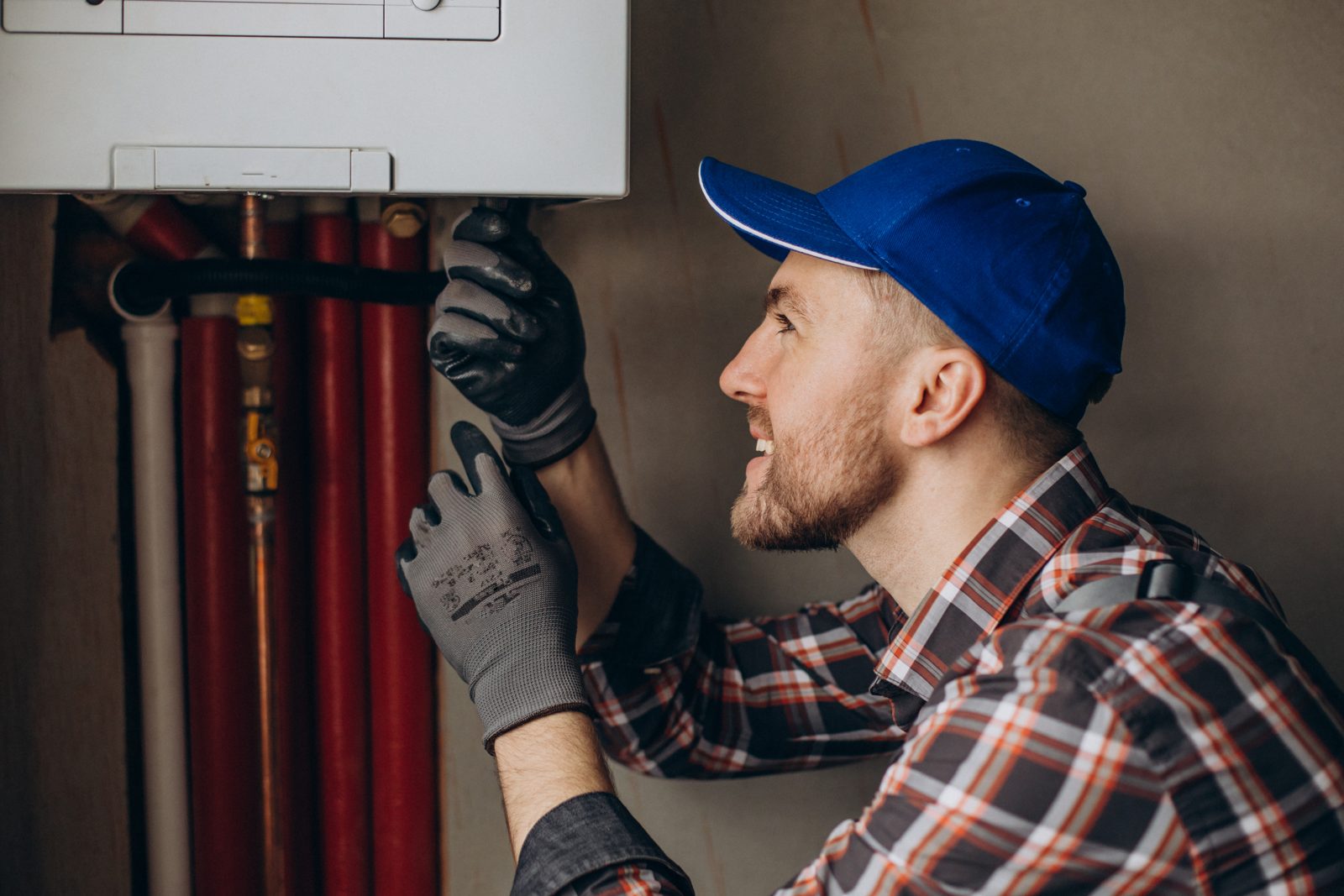 Heating engineer adjusting the pipework beneath a wall-mounted gas boiler